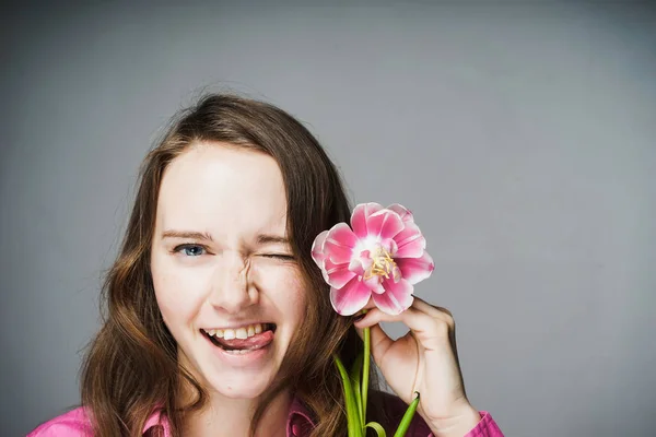 Leende blåögda flicka i en rosa skjorta som innehar en väldoftande blomma — Stockfoto