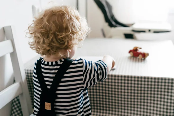 Curly malý chlapeček v kombinéze sedí u stolu v kuchyni a kreslení — Stock fotografie