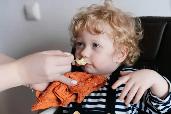 Добрая, заботливая мать кормит своего маленького кудрявого мальчика вкусным супом — стоковое фото