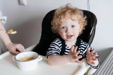 Mutfakta bir sandalyede oturup, bir yemek için bekleyen ve gülümseyen Kıvırcık sarışın mavi gözlü çocuk