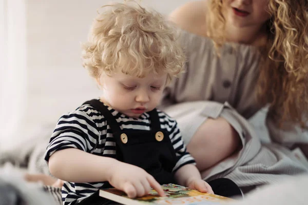 Una joven madre pasa tiempo con su pequeño hijo, le enseña a leer — Foto de Stock