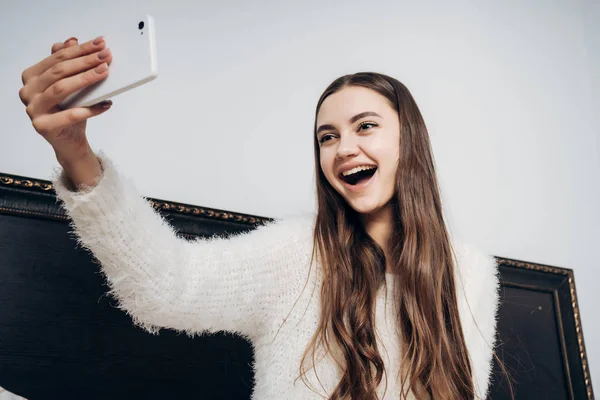 Radosny długowłosy młoda dziewczyna obudziła się wczesnym rankiem, uśmiechając się i podejmowania selfie na swoim smartfonie — Zdjęcie stockowe