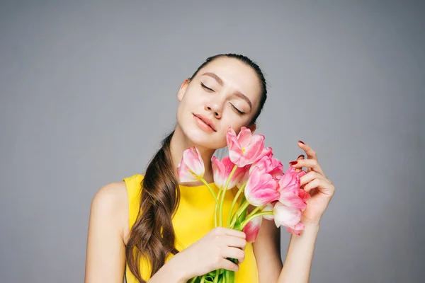 Sarı elbiseli güzel genç kız güzel kokulu pembe çiçekler sahiptir ve baharda, gözleri kapalı — Stok fotoğraf