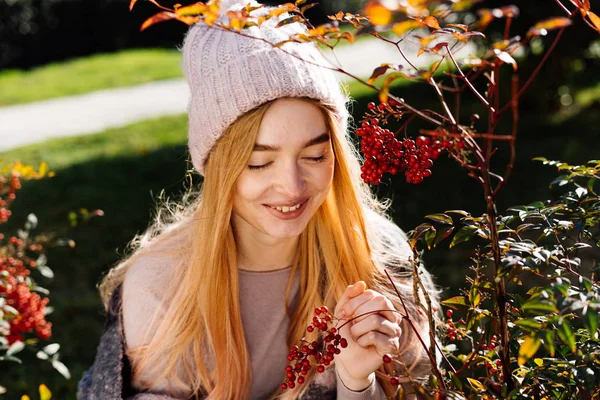 Glimlachend mooie jonge blonde vrouw in een warme muts wandelen in de tuin, genieten van de warmte en zon — Stockfoto