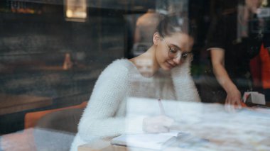 bir beyaz kazak ve gözlük çalışan, Genç kadın serbest meslek yazıyor onun defter, bir kafede