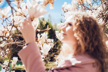 zarif kıvırcık kadının güneş ışınlarının bir parkta çiçek açan bir Manolya kokusu