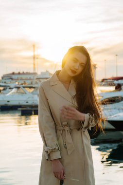 gün batımında liman içinde poz moda bej bir palto şık uzun saçlı kız