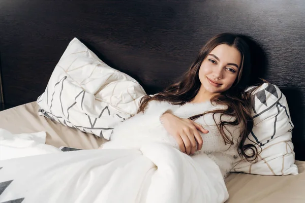 Hermosa joven se encuentra en la cama, descansando después de un día de trabajo y sonriendo — Foto de Stock
