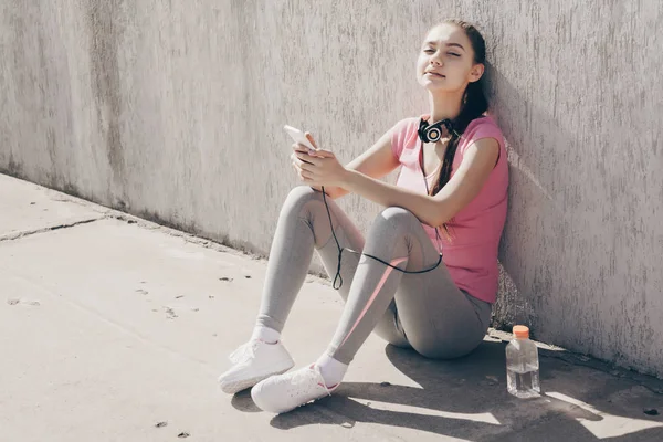 spor giyim sakin genç kız açık havada, yerde oturuyor dinlenme ve kulaklıklar müzik dinlemek