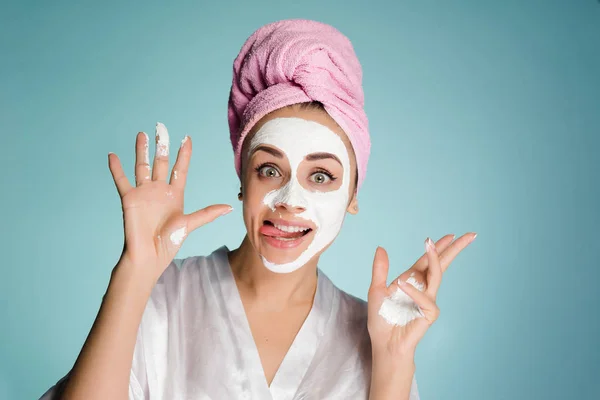 Una joven divertida con una toalla rosa en la cabeza cuida de sí misma y quiere ser hermosa, se pone una crema blanca en la cara — Foto de Stock