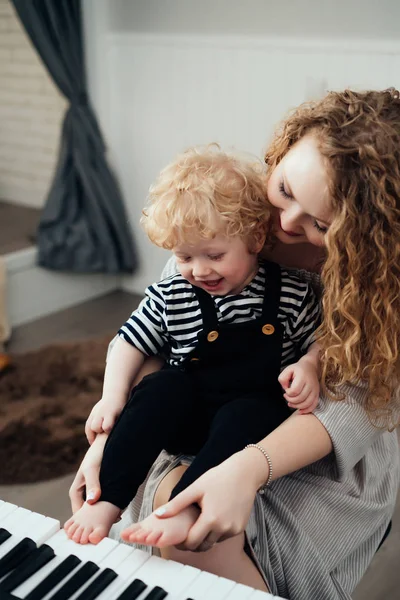 Curly young mother teaches her little boy child son to play the piano, laugh — Stock Photo, Image