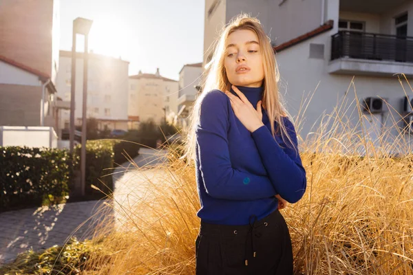 Впевнена стильна блондинка в синьому светрі позує на відкритому повітрі на сонці — стокове фото