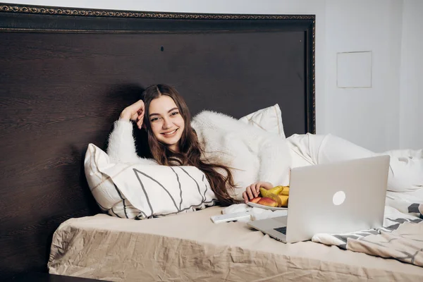 Een lachende jong meisje in pyjama ligt in bed's avonds kijken naar een interessante film op haar laptop — Stockfoto