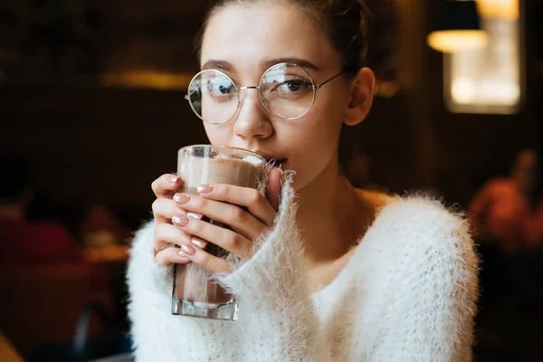 Милий молода дівчина студент в окулярах п'є запашний латте в кафе, відпочиває після навчання — стокове фото