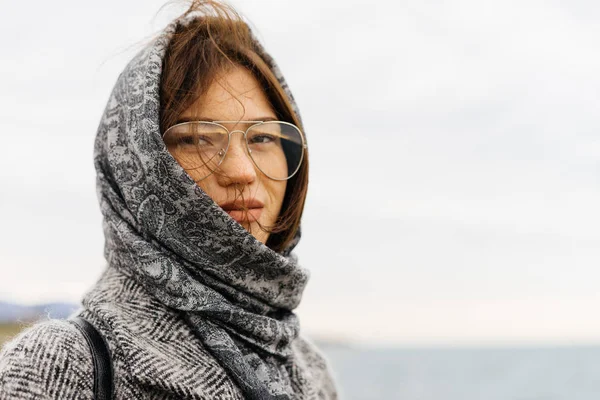 Молода стильна брюнетка дівчина в окулярах і сіре пальто насолоджується видом на море, позує — стокове фото