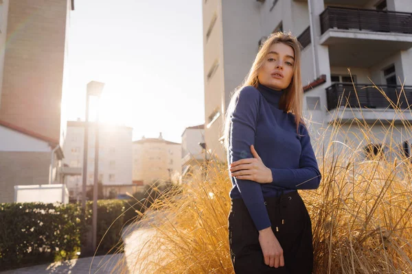 Vertrouwen stijlvolle meisje blond model in blauwe trui poseren op de straten van de stad in de zon — Stockfoto