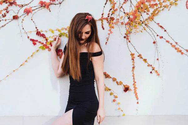 Atractiva mujer de pelo largo en un vestido negro costoso posando contra la pared en su jardín, descansando — Foto de Stock