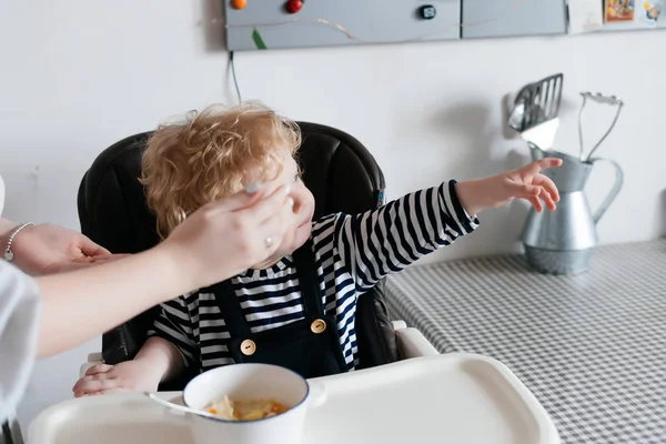 Мама кормит своего маленького мальчика вкусным супом на кухне, семейным завтраком — стоковое фото