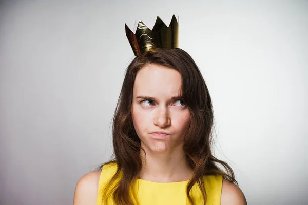 Descontenta joven pensativa en un vestido amarillo piensa en algo, en su cabeza una corona de oro — Foto de Stock