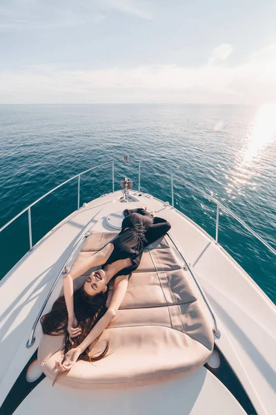Счастливая девушка в стильной черной одежде лежит на своей яхте, наслаждается отдыхом и морем — стоковое фото
