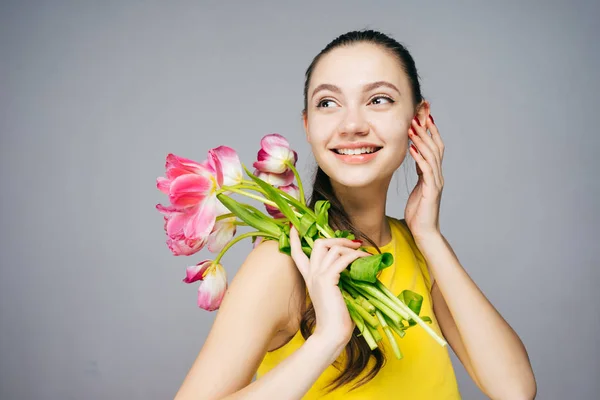 Cute young girl enjoying the spring in a yellow dress, holding fragrant pink flowers and smiling — Stock Photo, Image