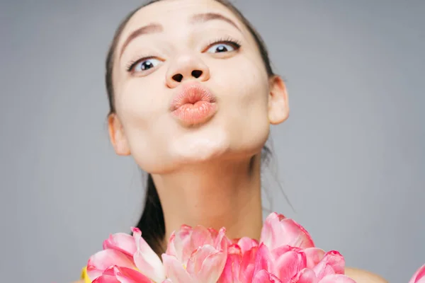 Забавная молодая девушка держит ароматные розовые цветы и посылает воздушный поцелуй — стоковое фото