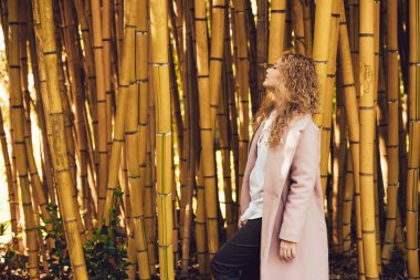 Bambu ağaçları yanındaki parkta poz trendy pembe ceket şık genç kadın