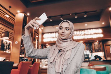güzel genç Arap kız hijab rahat bir restoranda onun Smartphone cep telefonu ile selfie yapar