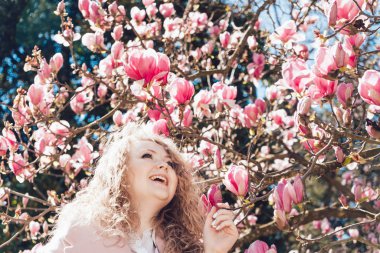 neşeli kıvırcık kadın parkta güzel kokulu bir çiçek açan Manolya sahiptir, bahar seviyor