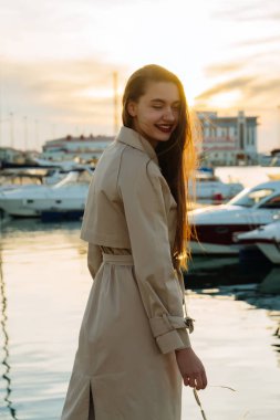 uzun saçlı kız moda bej bir palto akşam güneşi deniz poz gülümseyen