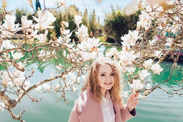 Happy curly woman enjoying body and spring in park next to pond and magnolia — Stock Photo, Image