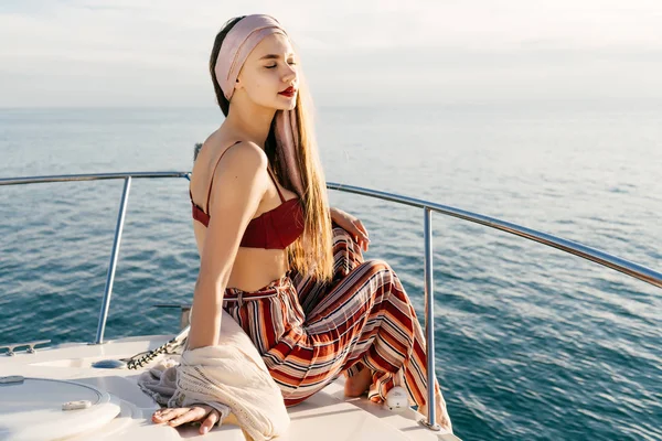 An attractive stylish girl in fashionable pants sits on a boat in the sun, relaxes and relaxes — Stock Photo, Image