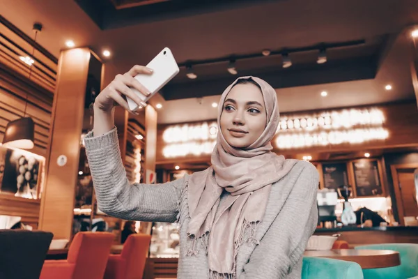 güzel genç Arap kız hijab rahat bir restoranda onun Smartphone cep telefonu ile selfie yapar