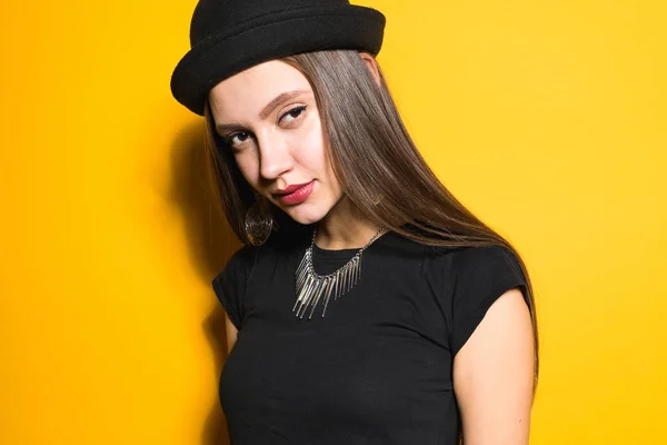 Jistý atraktivní model dívka v módní černý klobouk a šaty pózuje na žlutém podkladu — Stock fotografie