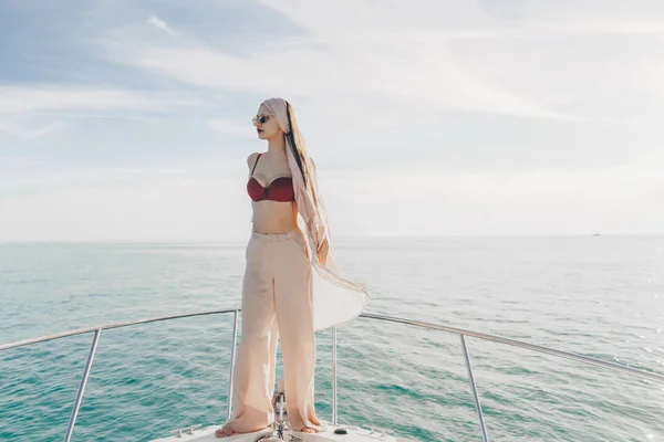 Joven chica con estilo en ropa de verano posando en su yate blanco al sol, disfrutando del viaje por el mar —  Fotos de Stock