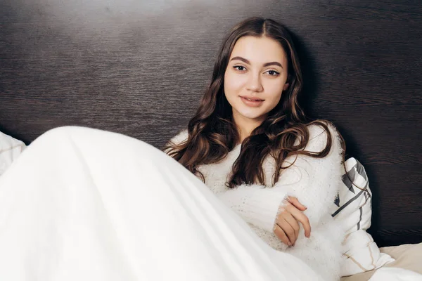 Hermosa chica somnolienta en pijama blanco se encuentra en la cama temprano en la mañana y no quiere levantarse — Foto de Stock