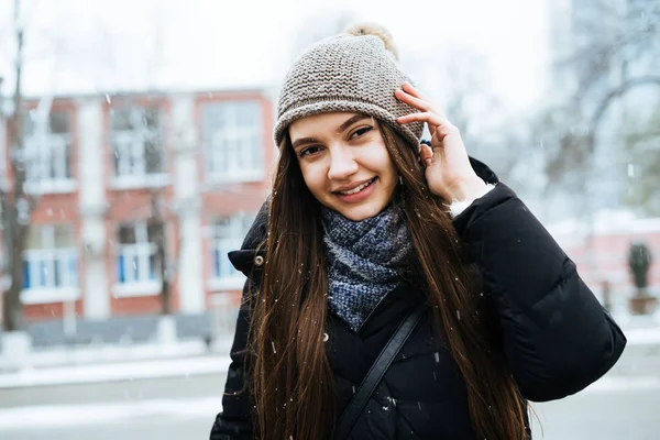 Bella giovane donna in una giacca calda e cappello cammina per le strade della città e gode della natura invernale — Foto Stock