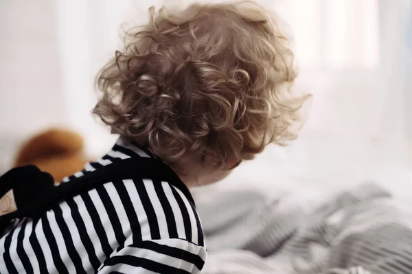 Kudrnaté blond malý chlapeček sedí na posteli hraje — Stock fotografie