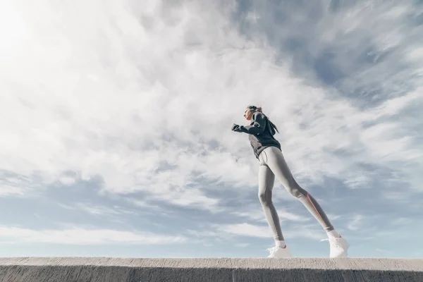 Уверенная в себе спортивная девушка, бегущая в голубом небе, готовящаяся к соревнованиям — стоковое фото