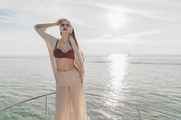 Una chica lujosa y elegante en ropa de verano disfruta de un viaje por el mar en un yate, en los rayos del sol —  Fotos de Stock