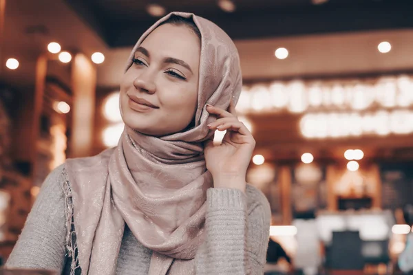 Hermosa chica árabe con pañuelo en la cabeza sonriendo, sentado en el restaurante y esperando su comida — Foto de Stock