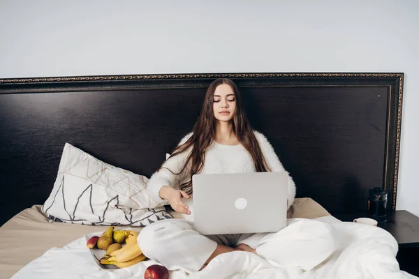 Пристрасна молода дівчина фрілансер сидить у ліжку, працює на своєму ноутбуці — стокове фото
