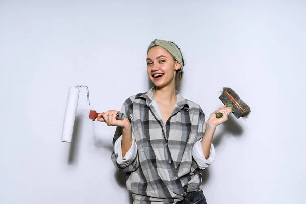 Счастливая улыбающаяся молодая девушка рисует стены с роликом и кистью в белом — стоковое фото