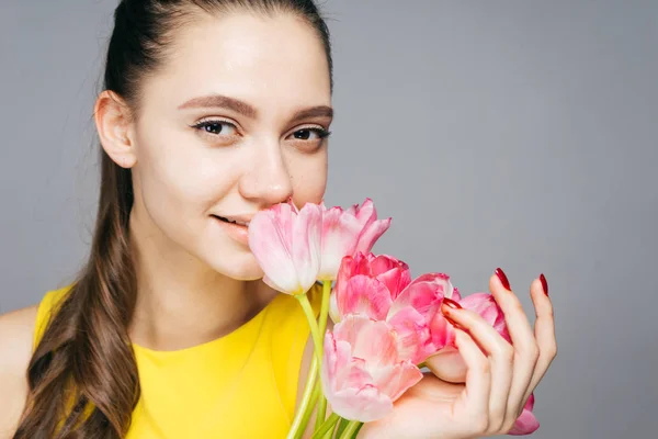 Leuk schattig meisje in een gele jurk ruiken een roze bloem en genieten van het voorjaar — Stockfoto