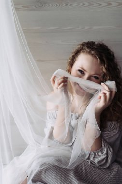 perde ile poz cam kenarında oturan güzel gülümseyen kıvırcık kadın