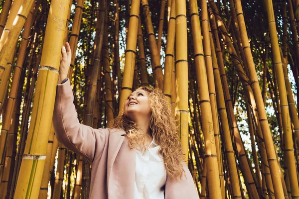 Joyful happy curly woman admiring the tall bamboo trees in the park in the spring — Stock Photo, Image