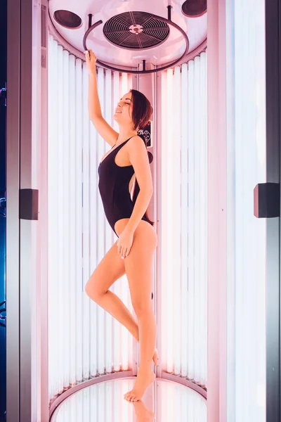 美丽迷人的女孩穿着黑色泳装想要一个美丽的鞣皮 站在一个日光浴沙龙 — 图库照片