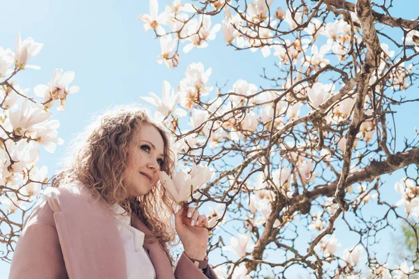 Mujer elegante encantadora huele la magnolia floreciente fragante en el parque, se planta con calor de primavera y sol — Foto de Stock
