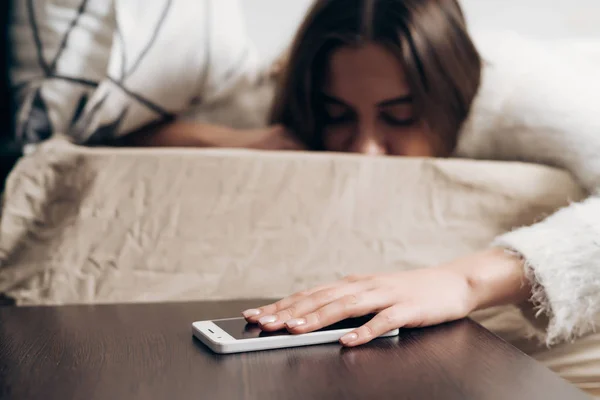 Sonnolenta ragazza si trova a letto la mattina presto, spegne l'allarme sul suo smartphone e non vuole alzarsi — Foto Stock