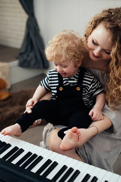 piyano çalmak, eğlenmek için küçük bebek oğlunun kıvırcık Genç Anne öğretir